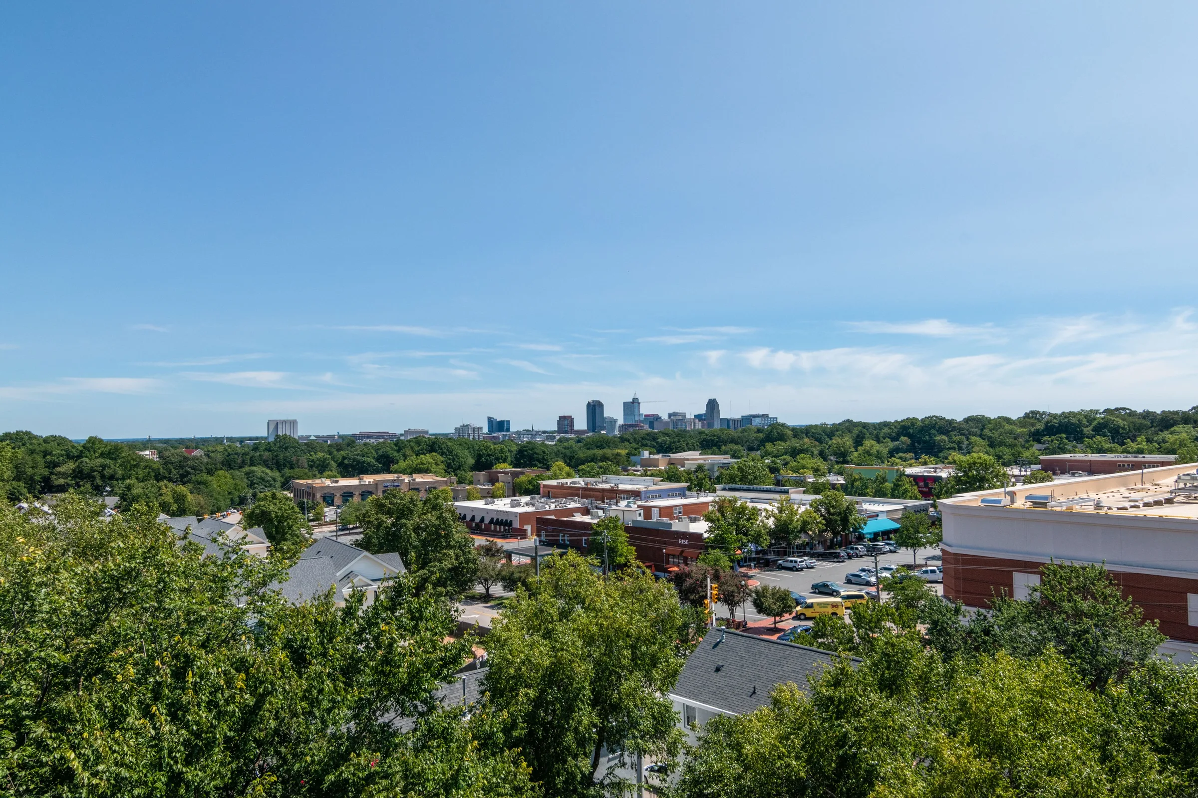 Aerial view of Decatur, Georgia commercial area with trees, buildings, and city skyline in distance.