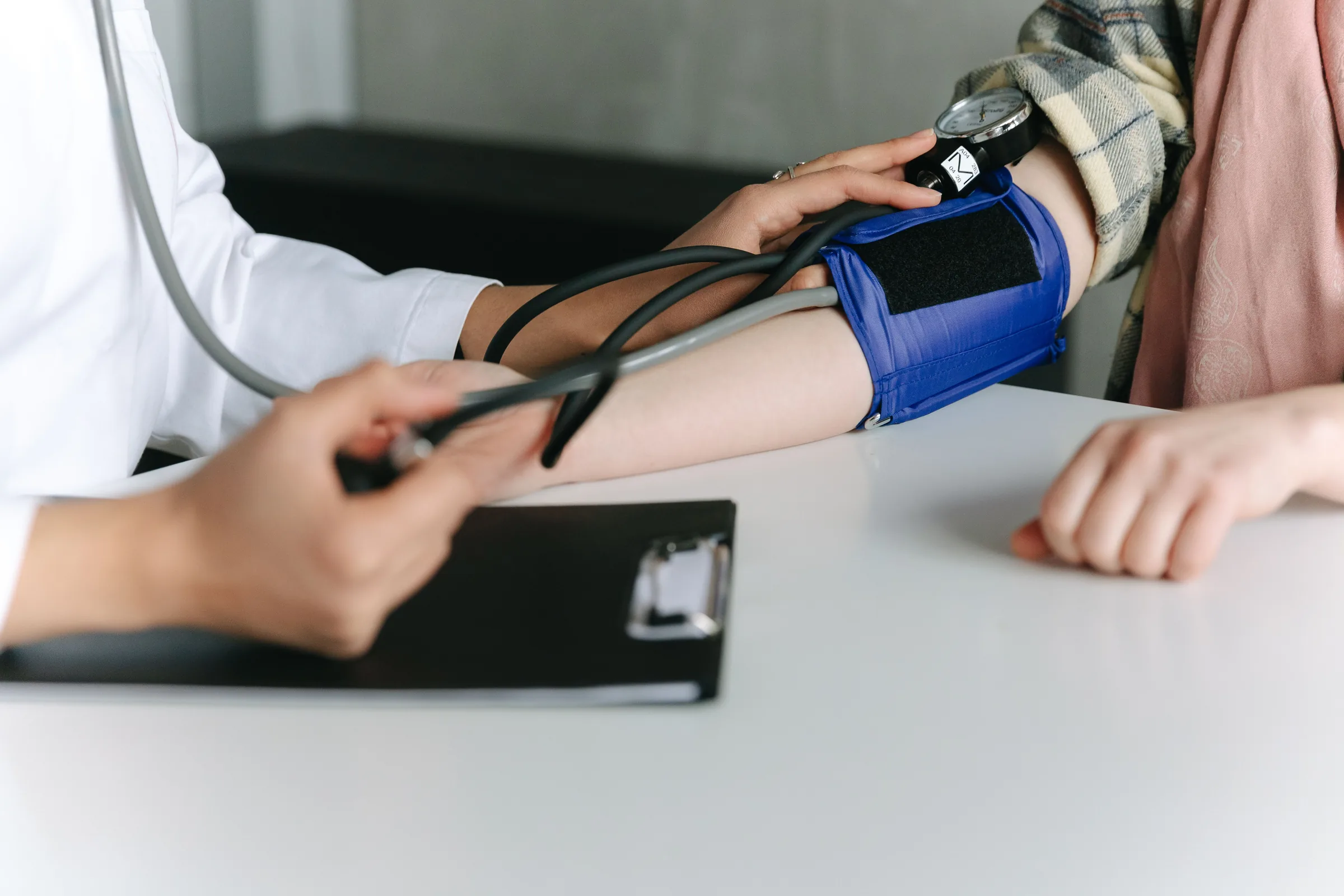 Healthcare provider measuring blood pressure on patient's arm with blue cuff during medical checkup.