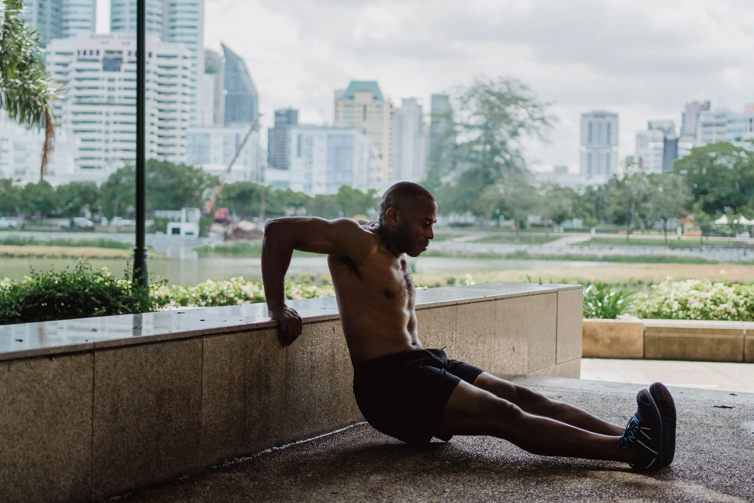 Man performing a tricep dip exercise on a concrete ledge with a city skyline in the background.