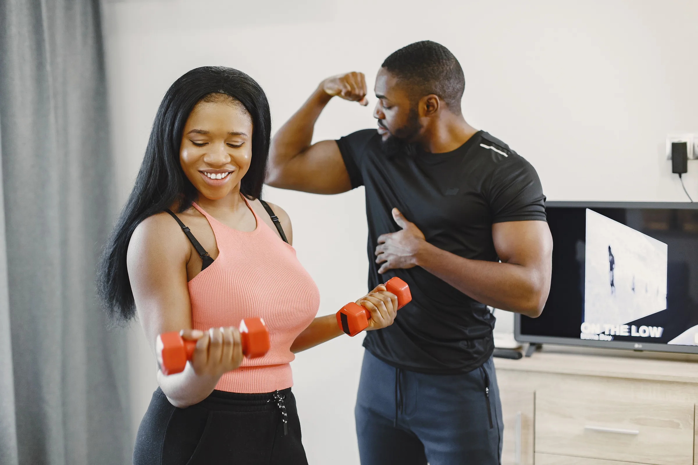 Personal trainer flexing bicep while woman holds dumbbells during weight loss training session.